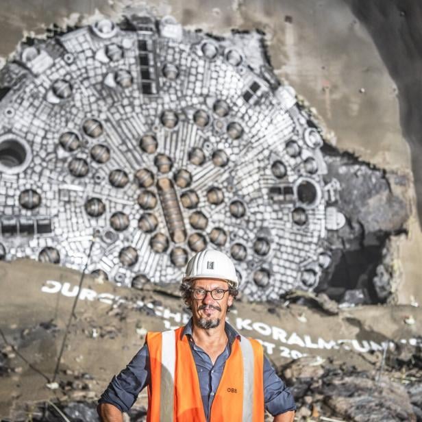 Ein Mann mit Bauhelm und in oranger Warnweste steht vor Tunnelbohrgerät