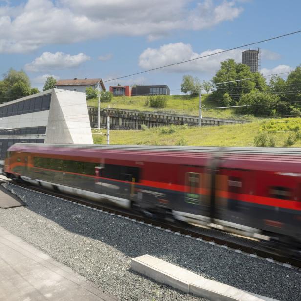 Roter Zug fährt an einem Tunnel und grünen Hügeln unter blauem Himmel vorbei.