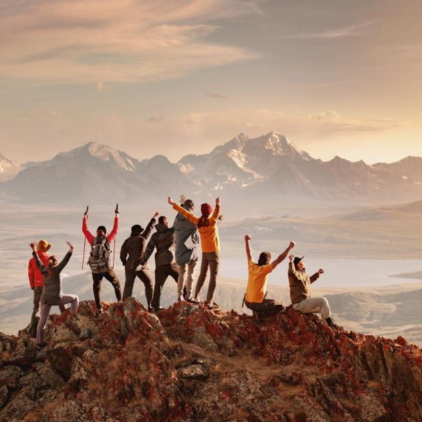 Mehrere Personen stehen auf einem Berggipfel und jubeln 