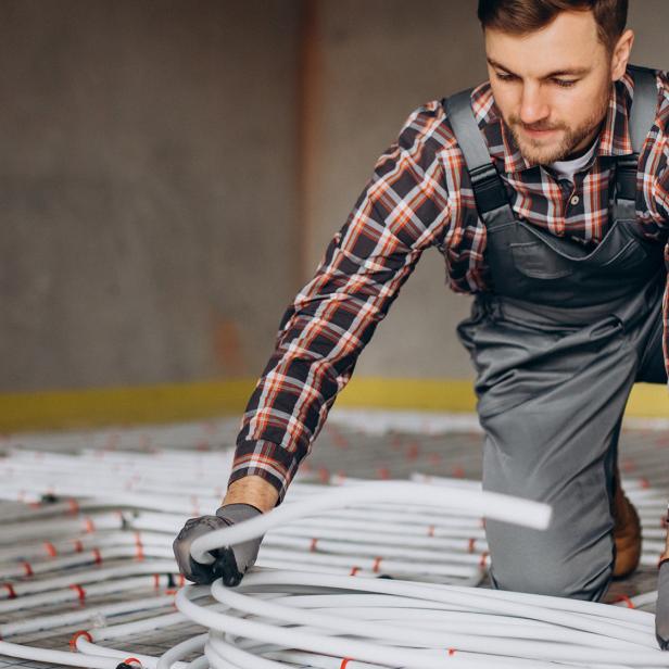 Handwerker verlegt weiße Rohre für eine Fußbodenheizung in einem Neubau.