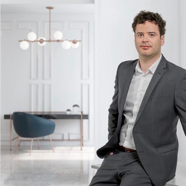 Mann im Anzug lehnt an einem Tisch in modernem, hell eingerichtetem Büro.