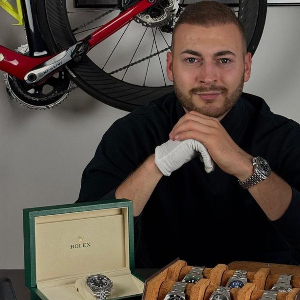 Mann sitzt vor mehreren Luxusuhren, darunter Rolex-Modelle in offenen Uhrenboxen.