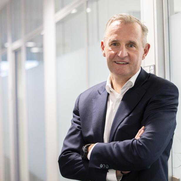 Peter Weinelt steht im Anzug mit gekreuzten Armen in seinem Büro.