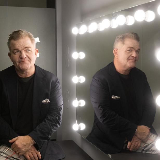 Ein Mann sitzt vor einem beleuchteten Spiegel und schaut nachdenklich, sein Spiegelbild ist deutlich zu sehen.