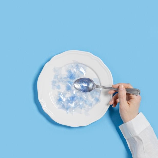 Ein Teller mit kleinen Mikroplastikteilchen und eine Hand, die einen Löffel hineinhält.