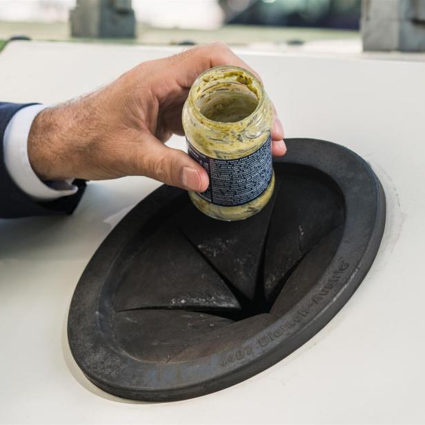 Eine männliche Hand wirft ein leeres Pestoglas in einen Glascontainer.