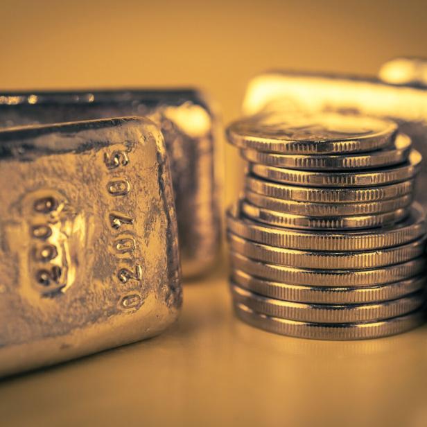 Mehrere Goldbarren und gestapelte Goldmünzen liegen nebeneinander auf einer glänzenden Oberfläche.