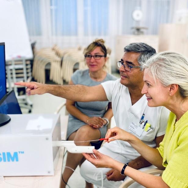 Drei Personen bedienen gemeinsam einen medizinischen Simulator und betrachten konzentriert den Monitor.
