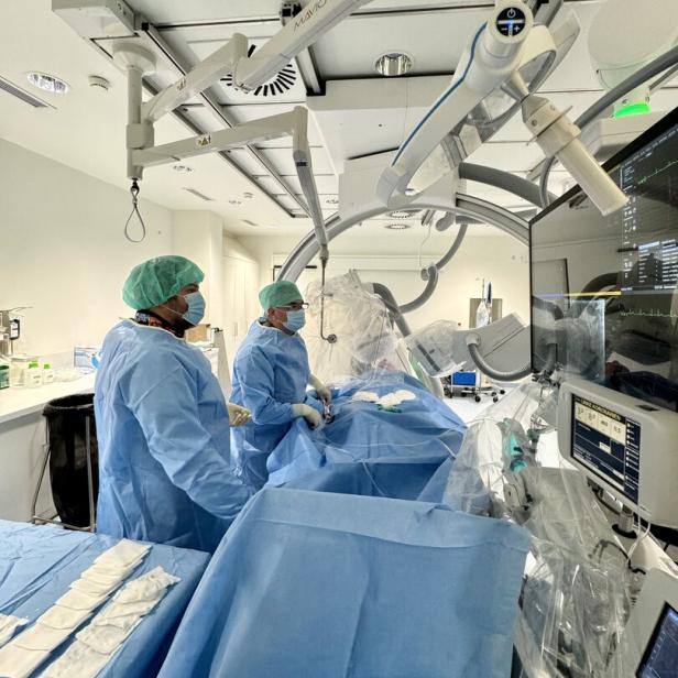 Zwei Personen in OP-Kleidung führen einen medizinischen Eingriff an einer liegenden Person mit moderner Technik durch.