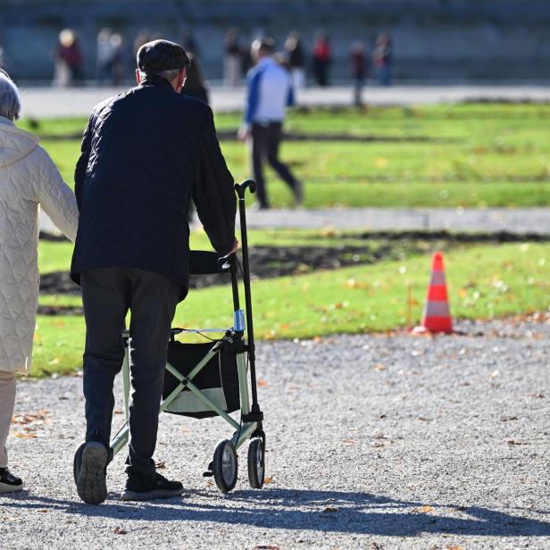 Ein älteres Paar geht im Park spazieren, der Mann mit einem Rollator.