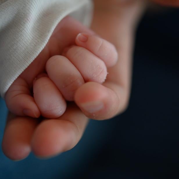 Eine kleine Babyhand umklammert einen Finger einer größeren Hand.