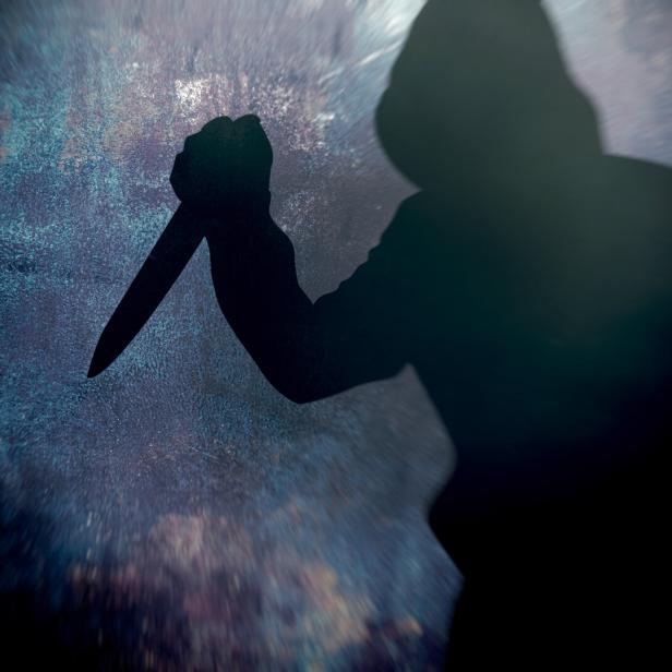 Eine dunkle Silhouette hält ein Messer vor einem gesprenkelten Hintergrund.