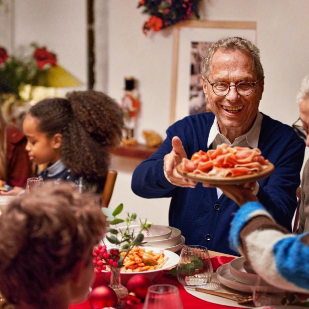Mehrere Generationen sitzen an einem festlich gedeckten Tisch und teilen gemeinsam Essen in fröhlicher Stimmung.