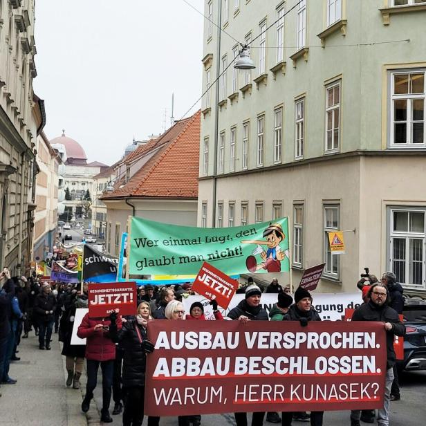 Demonstrierende Menschen mit Transparenten und Schildern ziehen durch eine enge Straße in einer Stadt.