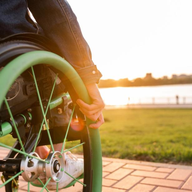 Eine junge Frau im Rollstuhl fährt am Ufer entlang und genießt die Sonne, Symbol für Selbstbestimmung trotz Friedreich Ataxie.