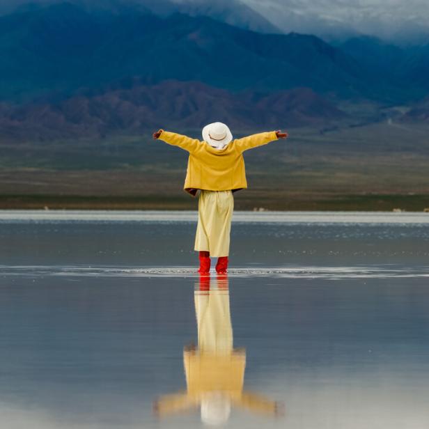 Eine Person steht mit Gummistiefeln knöcheltief in einem See, hat die Arme weit geöffnet und blickt hoffnungsvoll auf die vor ihr liegende Landschaft - und auf die Zukunft.