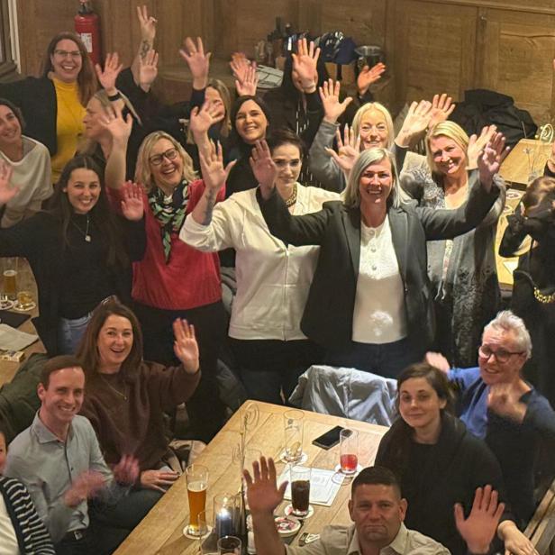 Gruppe von Menschen sitzt und steht in fröhlicher Stimmung in einem Restaurant und winkt.