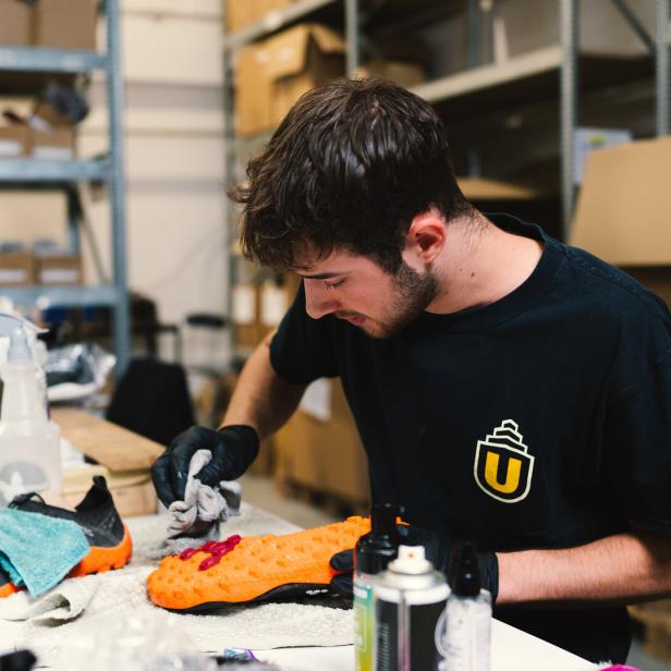 Ein Mann putzt ein Paar Schuhe mit unterschiedlichen Mitteln in einer Werkstatt