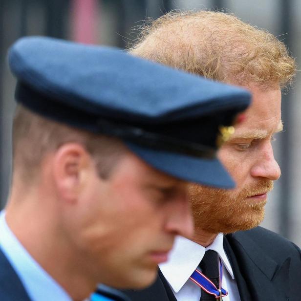 Prinz Harry steht neben Prinz William, beide mit gesenkten Köpfen.