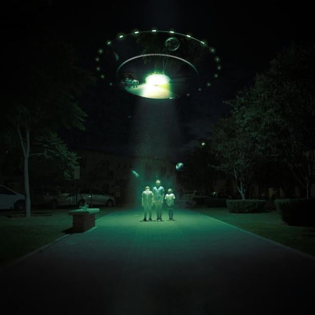 Ein UFO strahlt nachts eine Gruppe von Aliens auf einem Gehweg mit grünem Licht an.