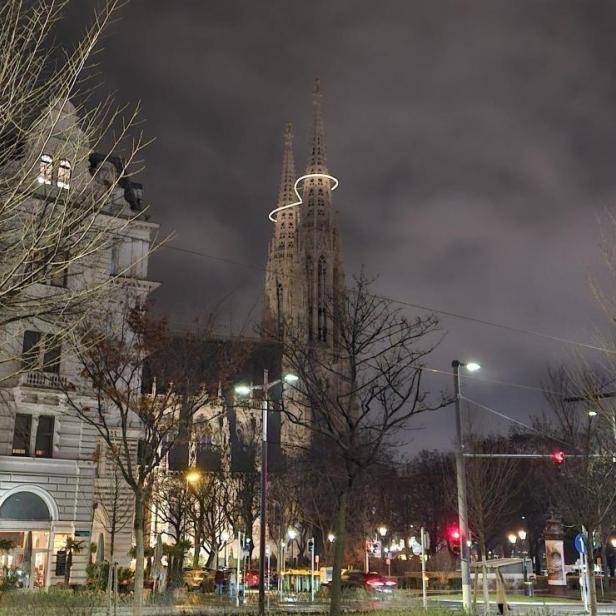 Die Votivkirche bei Nacht mit leuchtender Infinity-Lichtinstallation zwischen den Türmen.