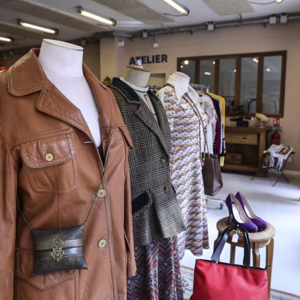 Drei Schaufensterpuppen mit Vintage-Kleidung und Accessoires stehen in einem hellen Laden, im Hintergrund läuft eine Frau vorbei.