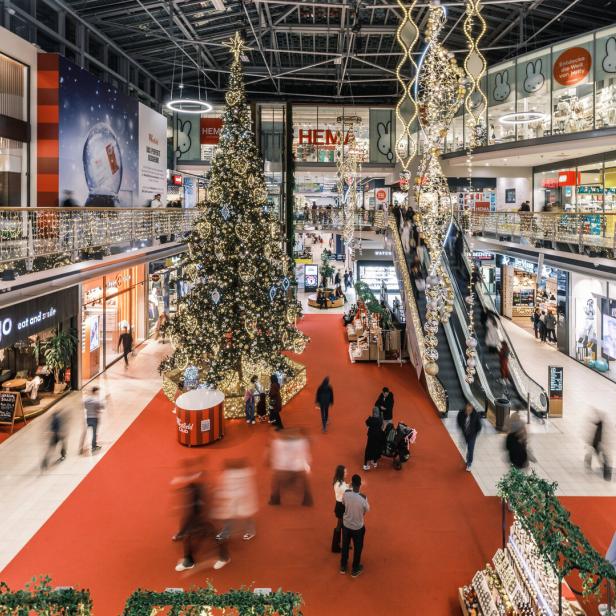 Großes Einkaufszentrum festlich mit Lichterketten und geschmücktem Weihnachtsbaum dekoriert, viele Menschen gehen einkaufen.