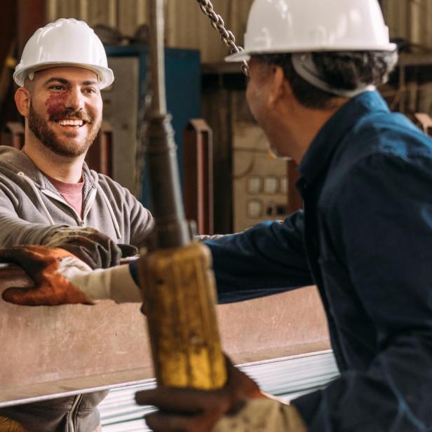 Zwei Männer mit Schutzhelmen unterhalten sich lächelnd.
