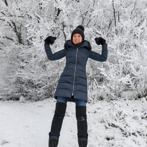 Eine Frau in einem Wintermantel im Schnee, die ihre Muskeln zeigt 