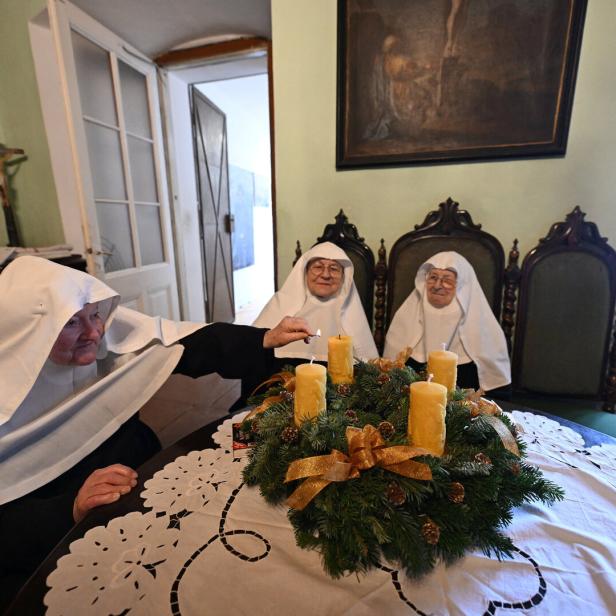 Drei Nonnen sitzen an einem Tisch mit Adventskranz und zünden Kerzen an.