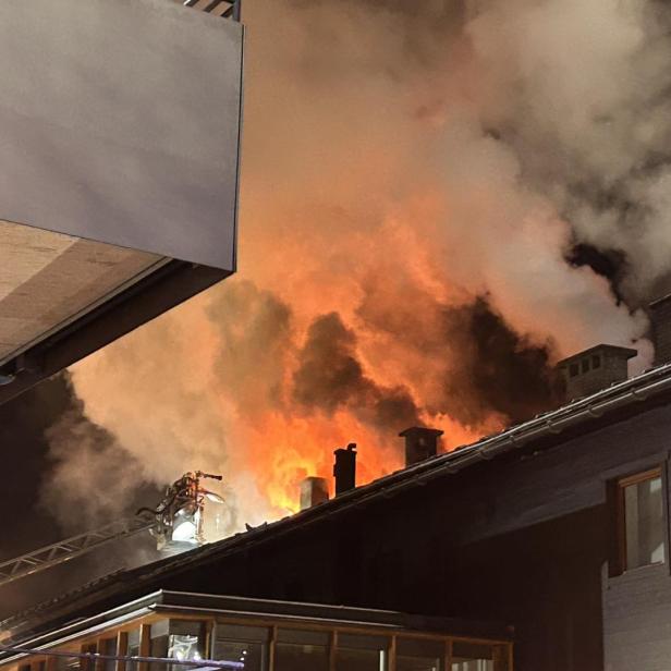 Flammen und dichter Rauch steigen aus dem Dachstuhl eines Gebäudes in der Nacht auf.