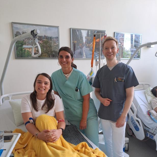 Katrin Teufel mit Besuchern in einem Bett im Krankenhaus.