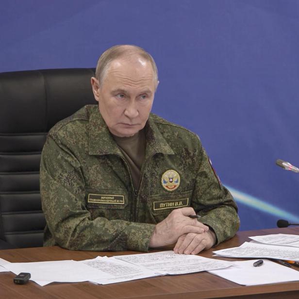 Putin sitzt in Uniform an einem Tisch mit Dokumenten und einem Mikrofon.