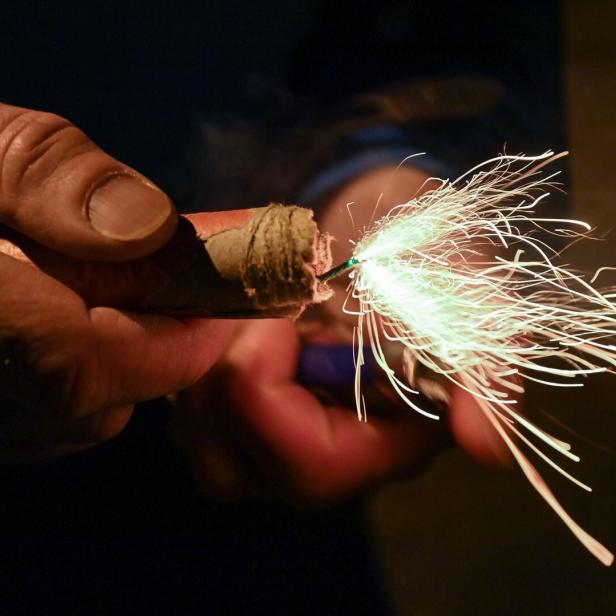 Eine Hand hält einen brennenden Böller, von dem Funken sprühen.