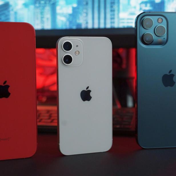 Drei iPhones in Rot, Weiß und Blau stehen nebeneinander vor einer Tastatur und Monitor.