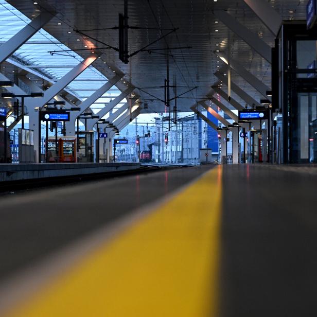 Ein leerer Bahnsteig mit gelber Sicherheitslinie und Anzeigetafeln unter einem modernen Dach.