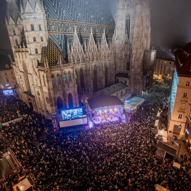 Große Menschenmenge versammelt sich bei Nacht vor einem beleuchteten Dom mit Bühne und Leinwand in einer Innenstadt.