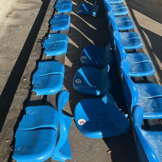 Mehrere blaue Kunststoffsitze in einer Stadionreihe sind beschädigt oder fehlen teilweise.