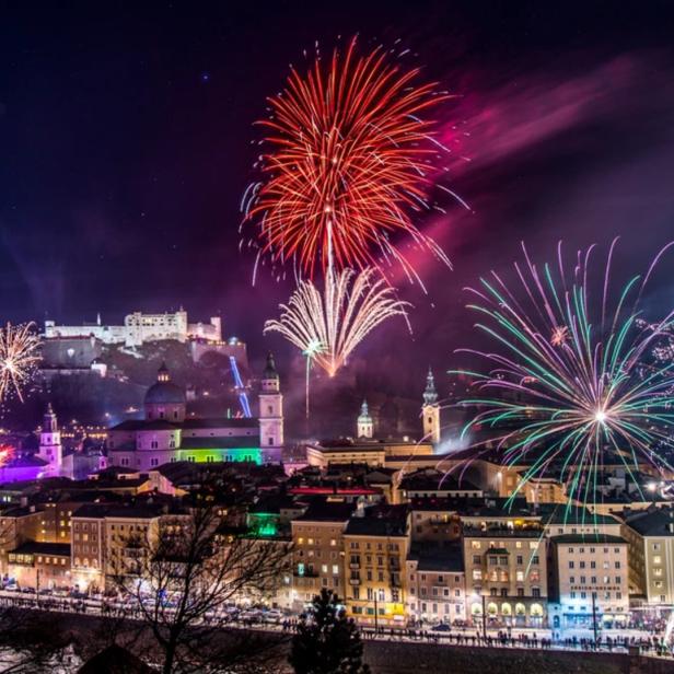 Über Salzburg leuchten bunte Feuerwerke am Nachthimmel, die Festung Hohensalzburg ist im Hintergrund erkennbar.