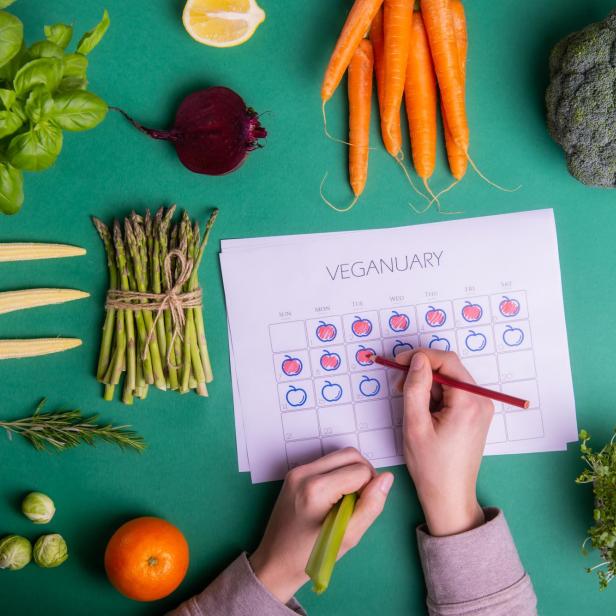 Verschiedene Gemüsesorten liegen um einen Kalender für Veganuary, in den eine Person mit einem Stift einträgt.