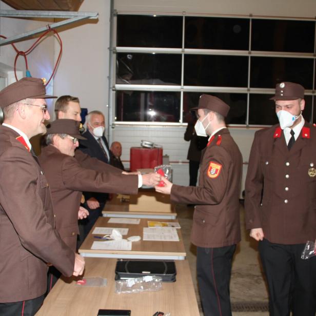 Feuerwehrmänner in Uniform übergeben sich gegenseitig ein verpacktes Geschenk.
