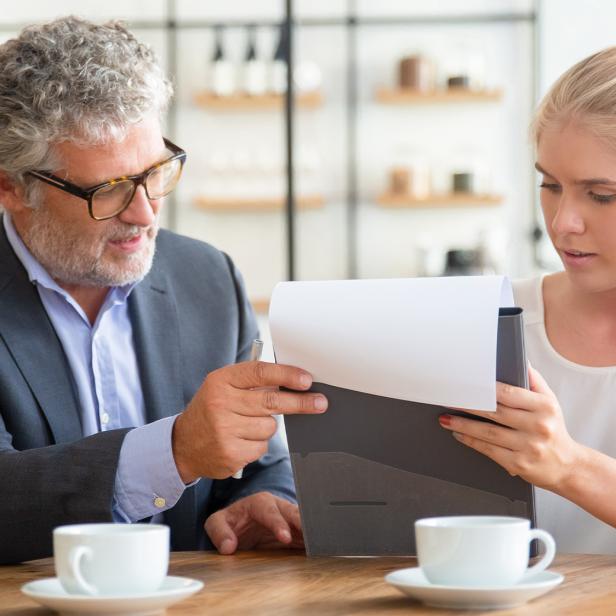 Eine junge Frau und ein Man sitzen an einem Tisch und sehen sich ein Dokument auf einem Klemmbrett an.