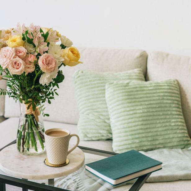 Coffee cup, flowers, and notebook on a glass table next to a couch