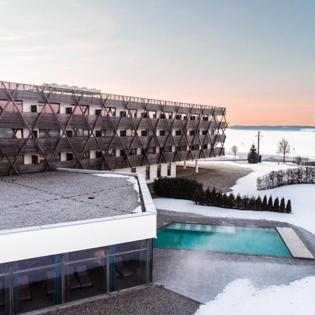 Ein Hotelgebäude mit großem Außenpool in winterlicher Landschaft mit Schnee.