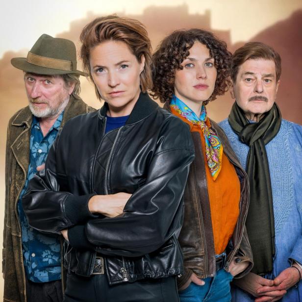 Vier Erwachsene stehen nebeneinander, jeder mit unterschiedlichem Gesichtsausdruck und individueller Kleidung.