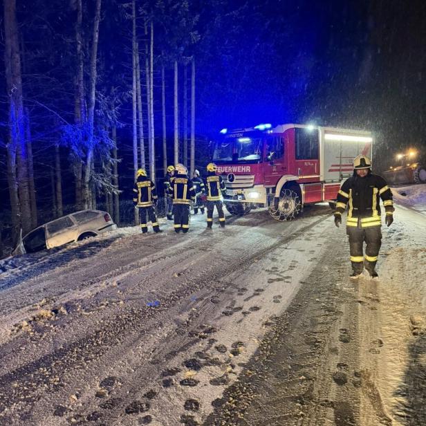 Feuerwehrleute sichern bei Nacht eine verschneite Straße, während ein Auto im Straßengraben liegt.