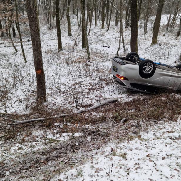 Ein Auto liegt am Dach zwischen Bäumen auf dem verschneiten Waldboden.