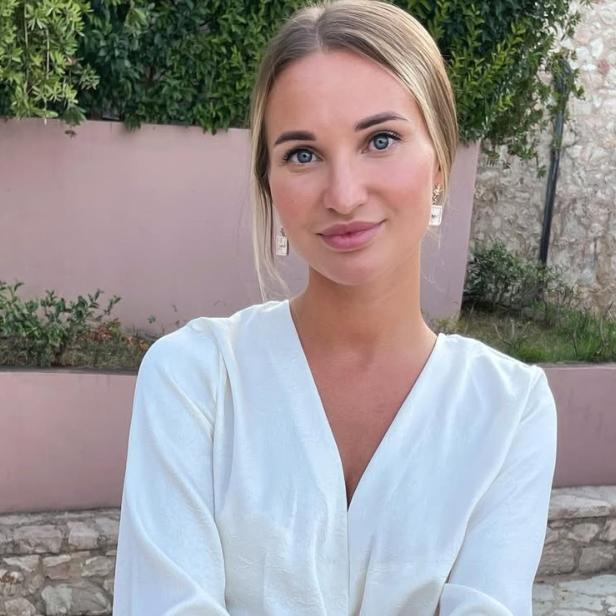 38-jährige blonde Frau mit weißer Bluse posiert lächelnd für ein Foto