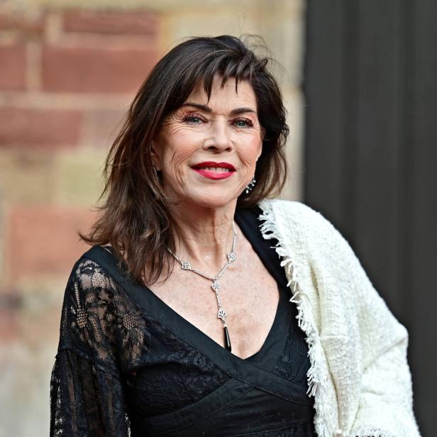 Frau mit dunklen Haaren trägt ein schwarzes Spitzenkleid, eine weiße Stola und eine silberne Halskette.