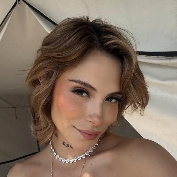 28-jährige Frau mit kurzen blonden Haaren lächelt in die Kamera für ein Selfie